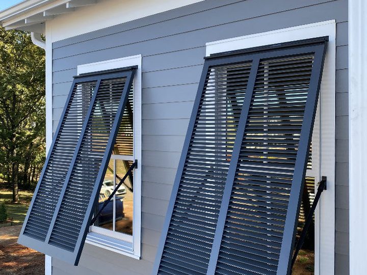 Two black Bahama shutters hinged at the top and propped open on gray lap siding