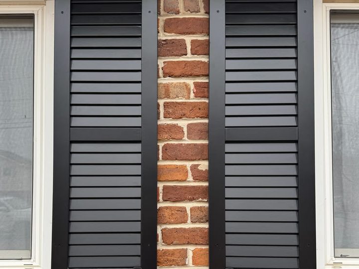 Black painted composite louvered shutters mounted on a red brick wall