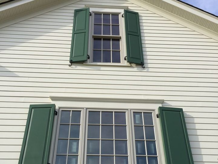 Dark green custom raised panel shutters on a white clapboard home